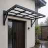 Marquesina de entrada en acero de estructura abierta, sobre la puerta de una casa enlucida bajo la lluvia