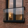 Balcon à la française avec verre maintenu en profilé, sur une façade en briques le soir